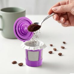 Hand adding coffee grounds to a purple reusable Keurig coffee filter pod.