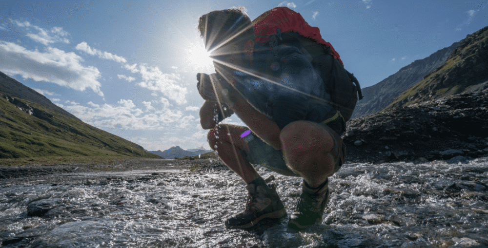 Hiker using water filter in mountain stream.