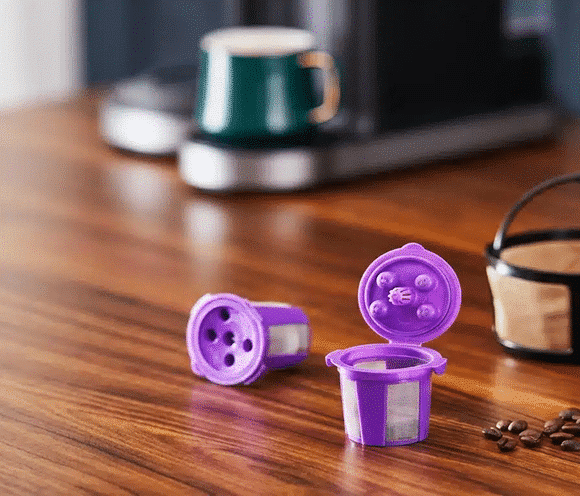Reusable K-Cups on a wooden table with a Keurig coffee maker in the background.