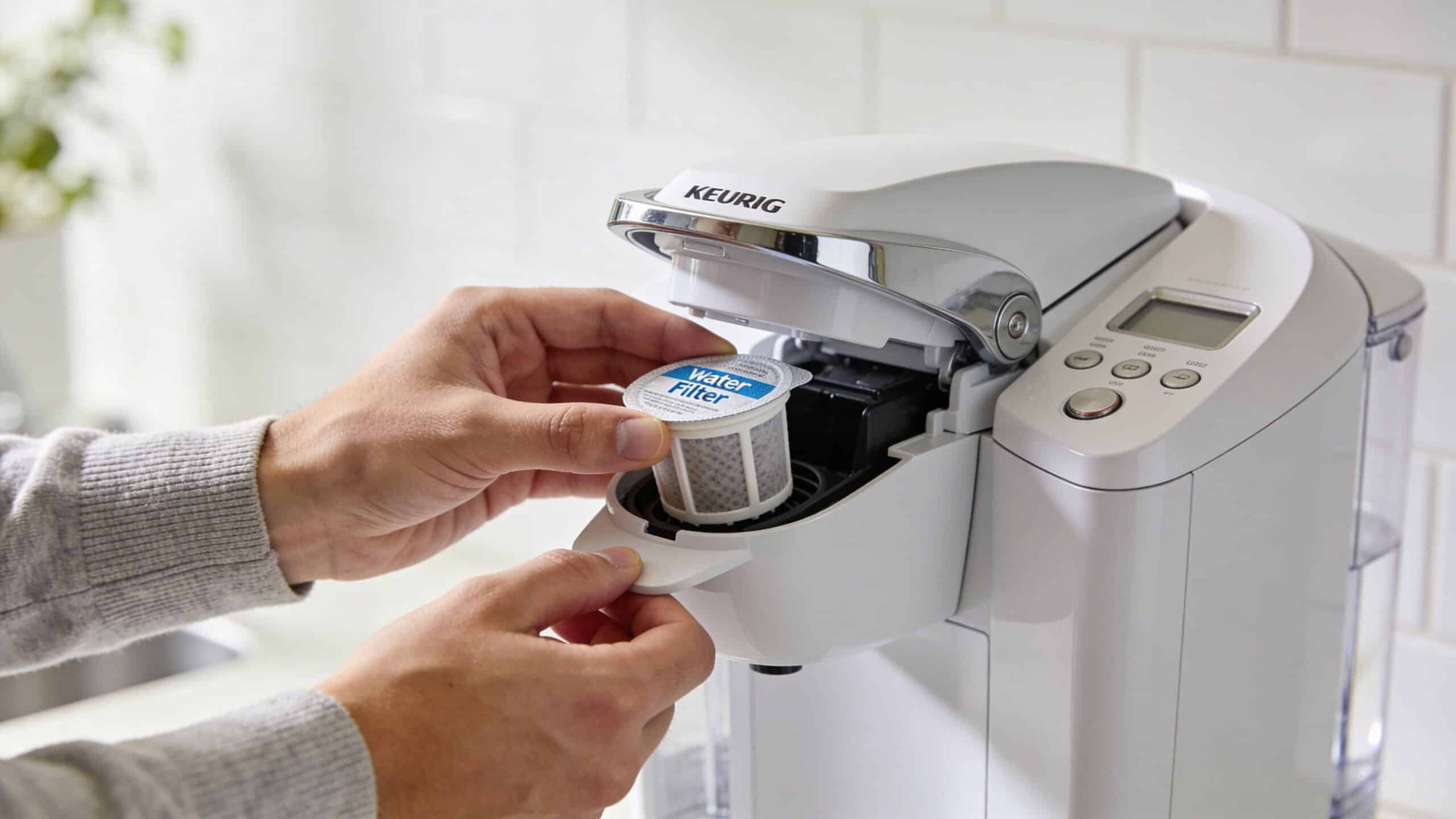 A close-up view of a person inserting a water filter cartridge into a Keurig coffee machine.