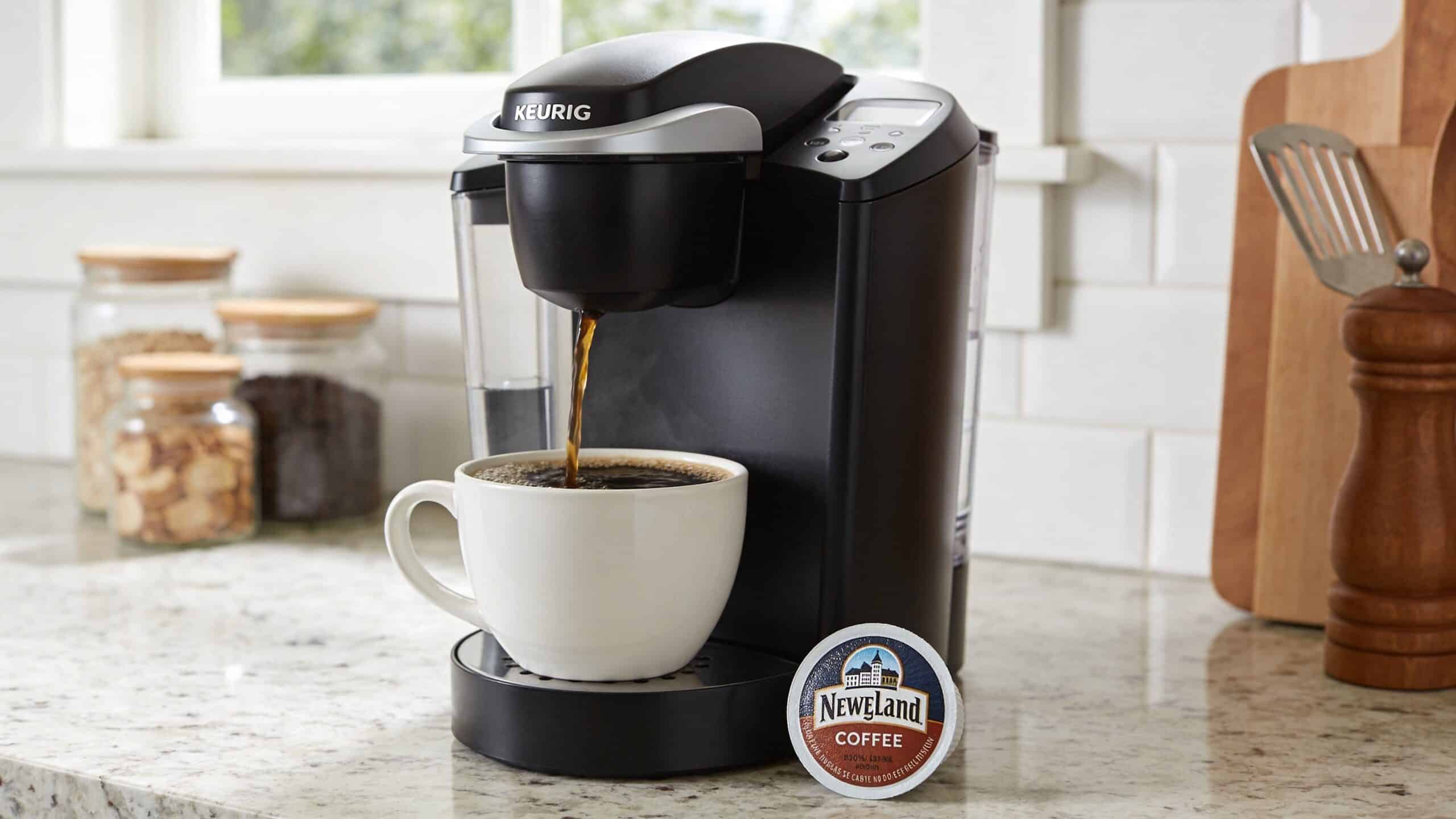 A black Keurig coffee machine pouring fresh hot coffee into a white ceramic mug on a kitchen counter.