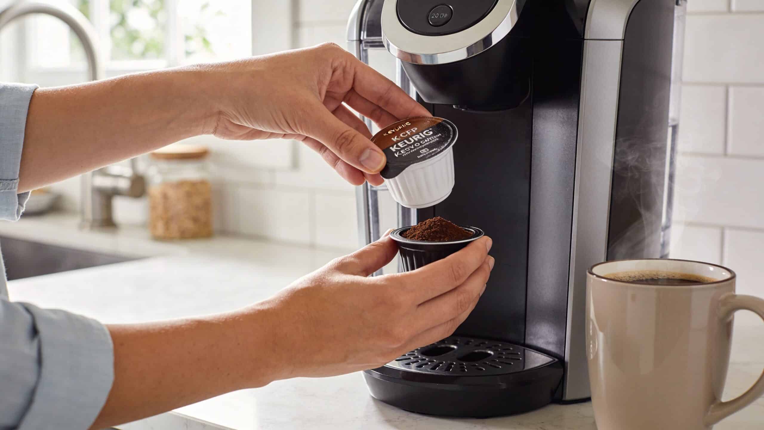 A person preparing to insert a refillable coffee pod into a Keurig coffee maker on a kitchen counter.