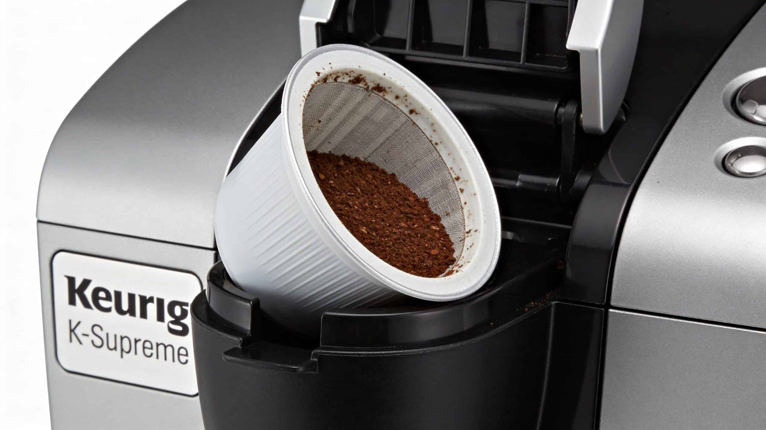 A close-up view of a reusable coffee filter pod sitting inside an open Keurig K-Supreme coffee maker.