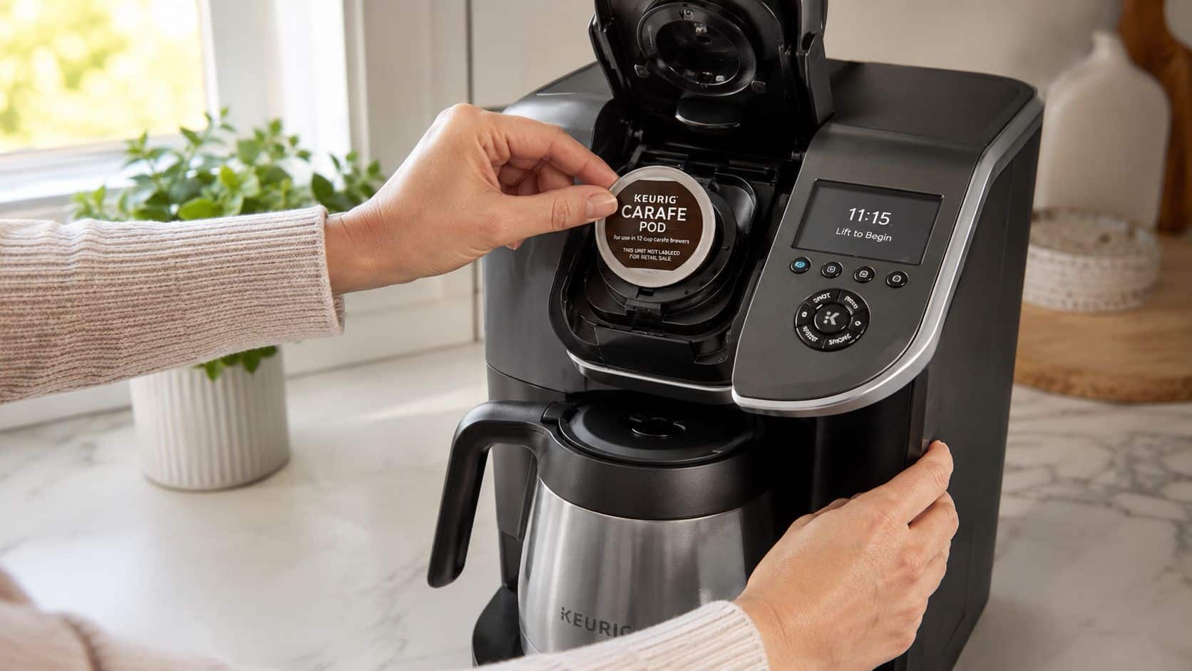 A person placing a Keurig carafe pod into a black Keurig coffee maker on a kitchen counter.
