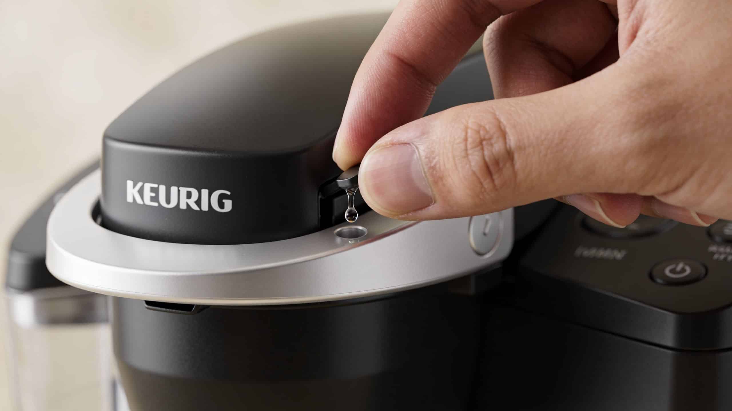 A hand carefully installing or inspecting a water filter holder on a black Keurig coffee machine.