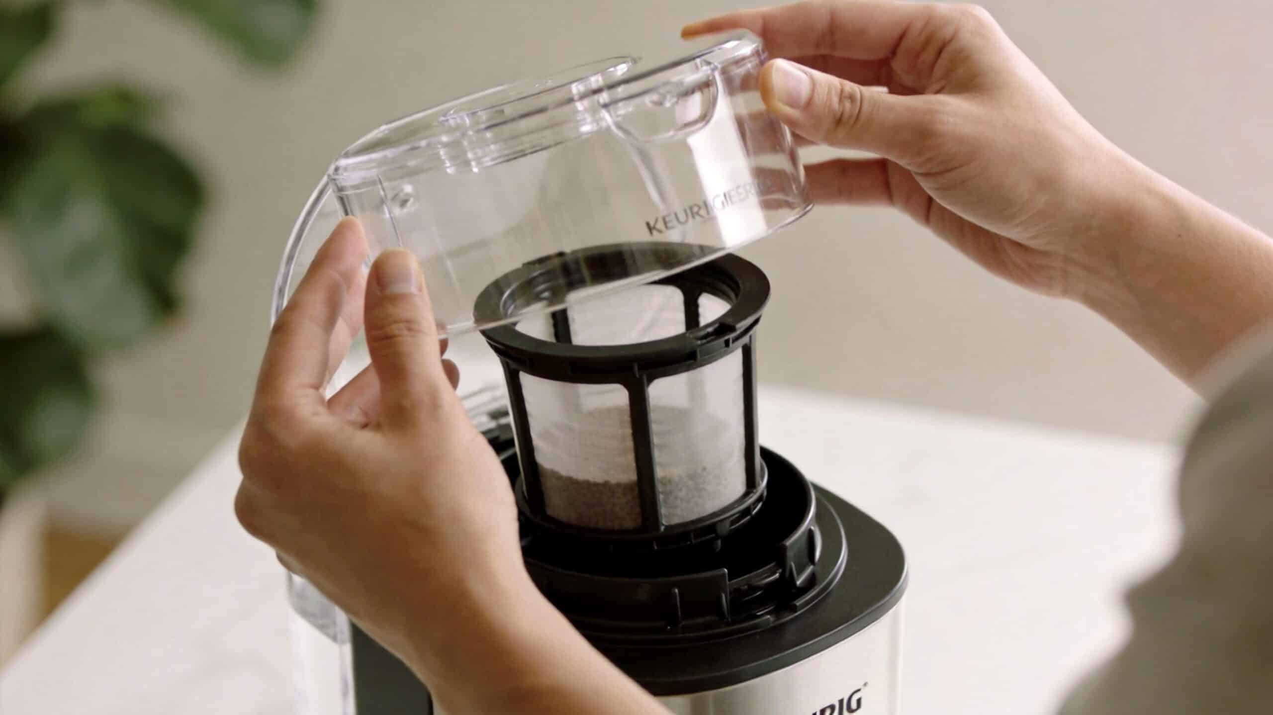 A person placing a clear plastic lid onto the reusable coffee filter basket of a Keurig machine.