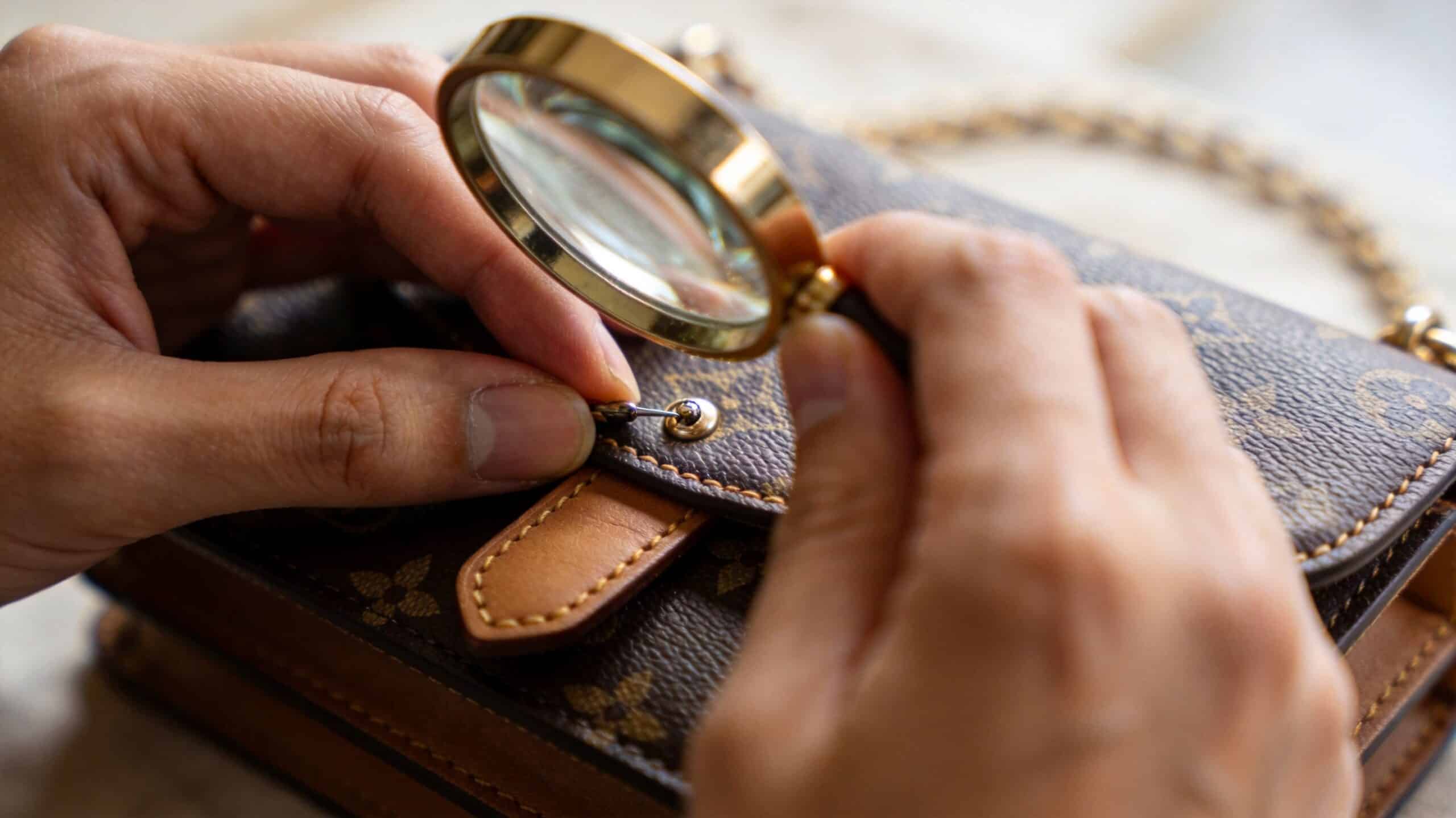 A professional inspector using a magnifying glass to verify the authenticity of a designer handbag.