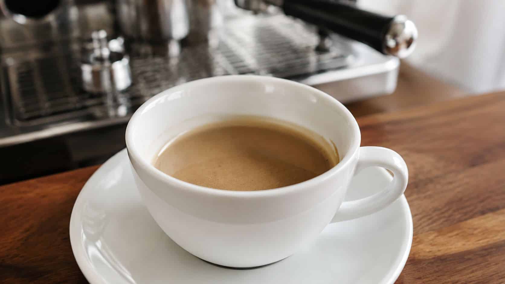 A cup of freshly brewed espresso sitting on a wooden surface next to an espresso machine.