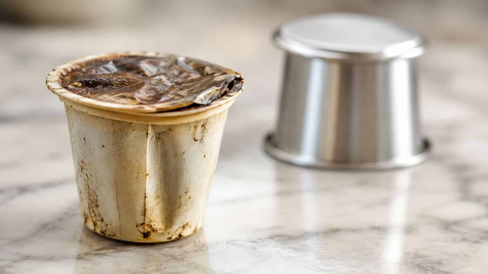A used disposable coffee capsule sitting on a marble countertop next to a clean metal container.