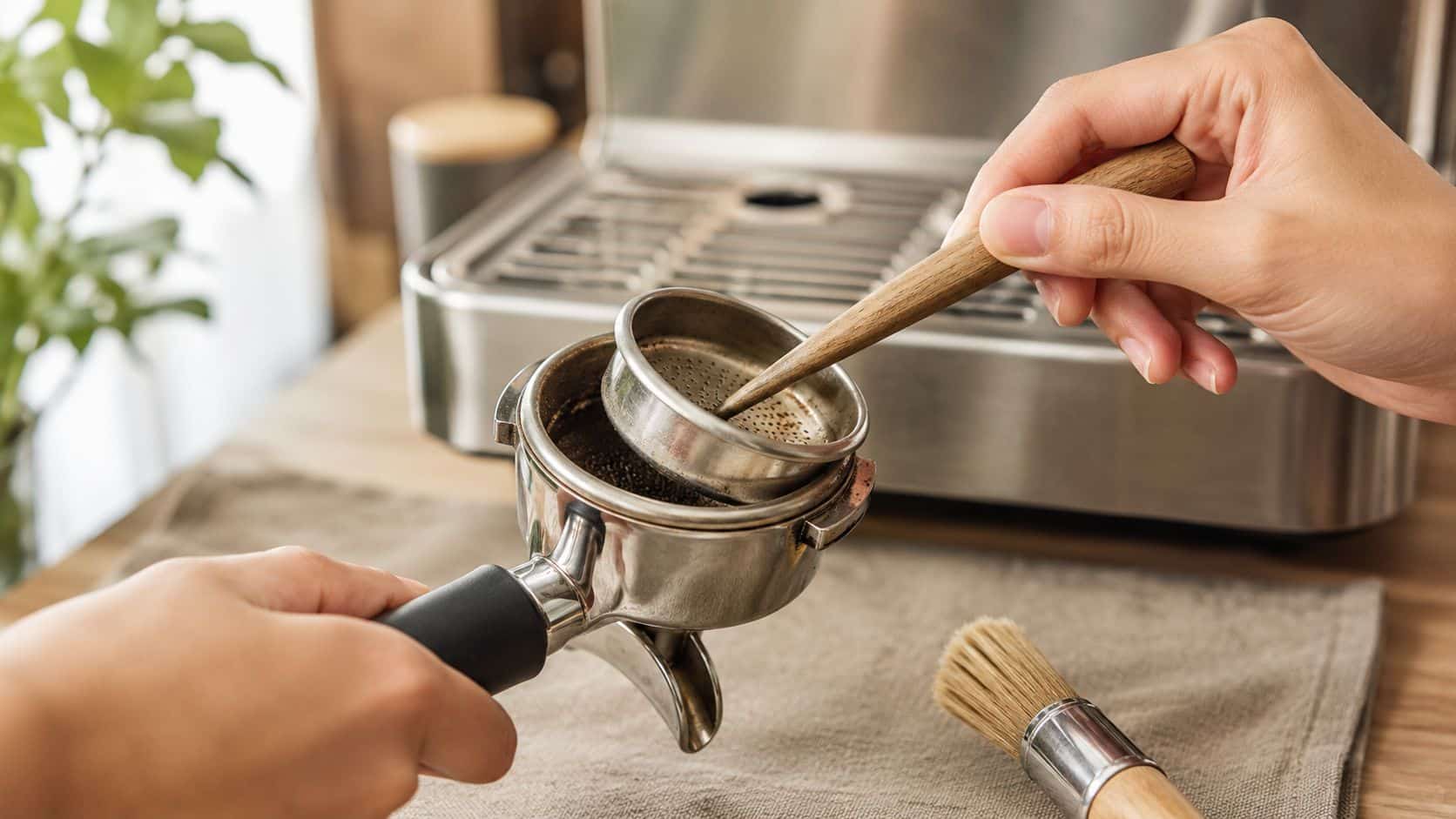A person preparing a portafilter by placing a coffee filter basket into the handle holder.