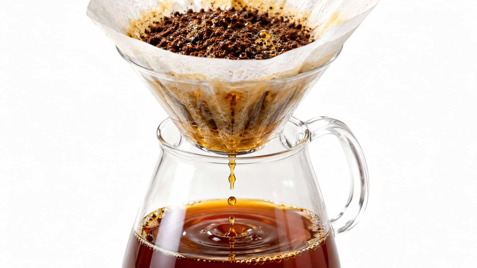 A close-up of fresh coffee dripping from a glass cone filter into a glass carafe below.