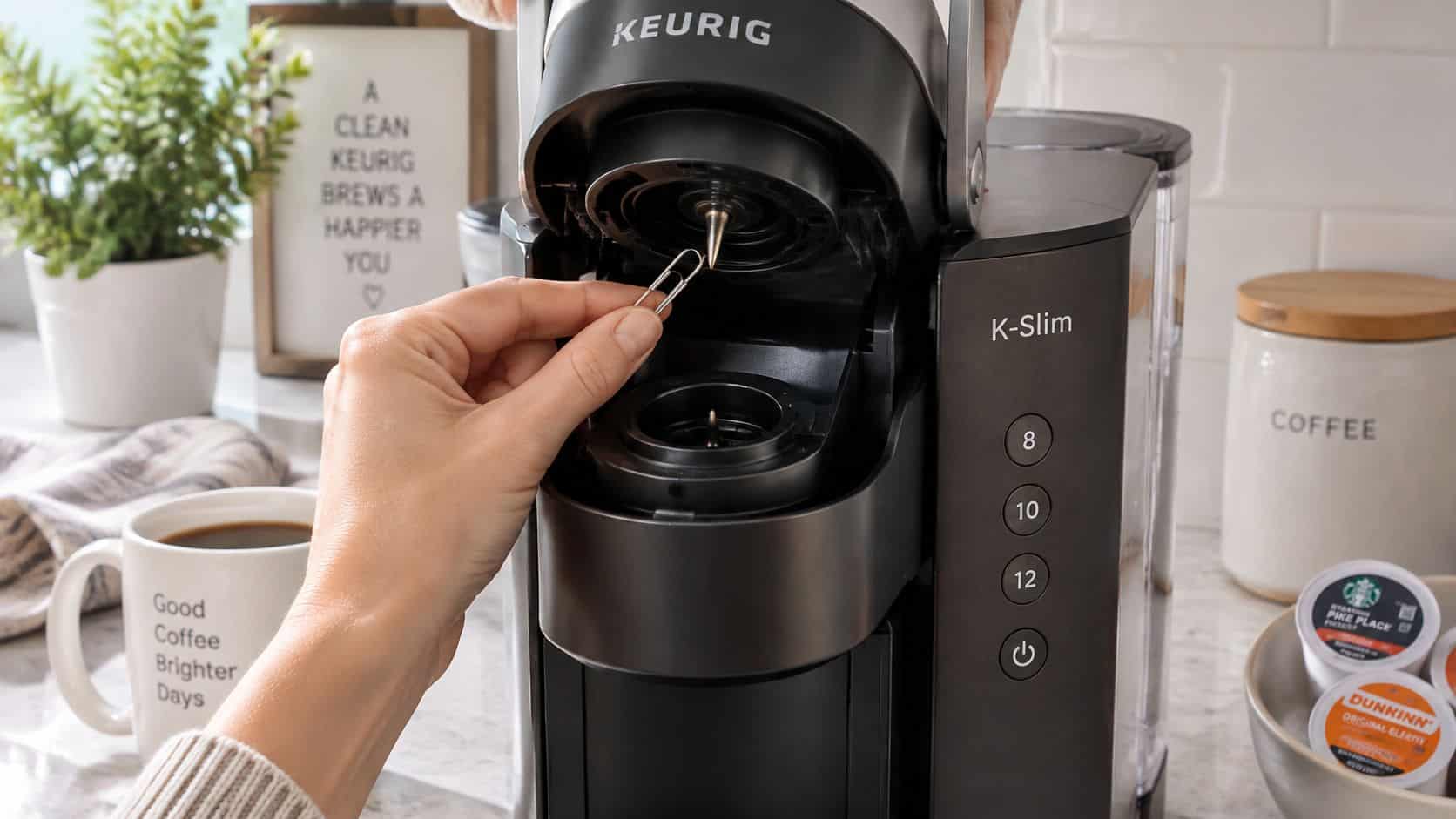 A person uses a paperclip to clear the needle of a Keurig K-Slim coffee maker.